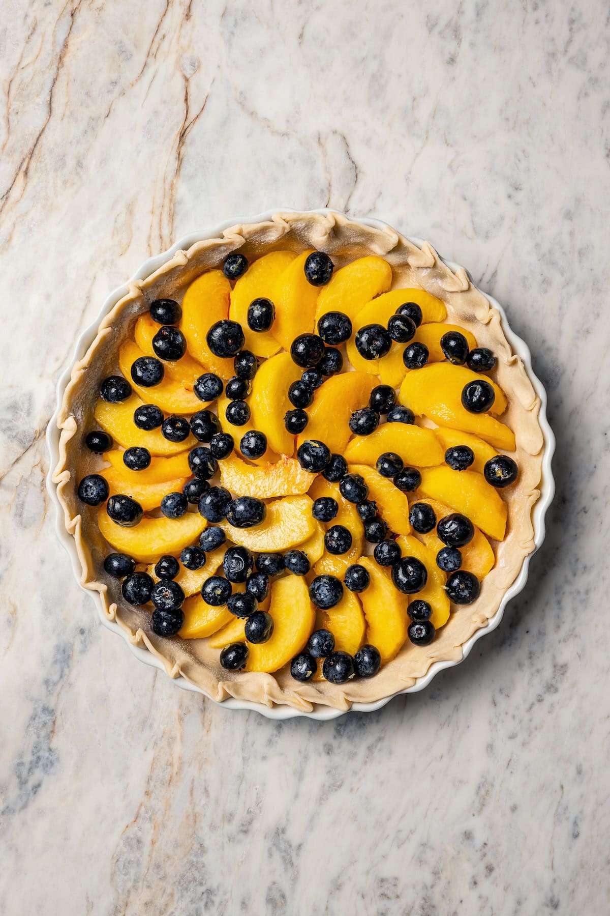 This peach blueberry pie is a fruit-filled custard pie bursting with juicy fresh peaches and blueberries, topped with a nutty pecan streusel. A pie crust filled with peach slices and blueberries.