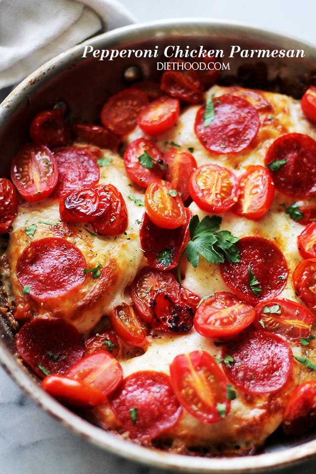 A skillet with cooked chicken breasts topped with melted cheese, slices of pepperoni, and halved cherry tomatoes.