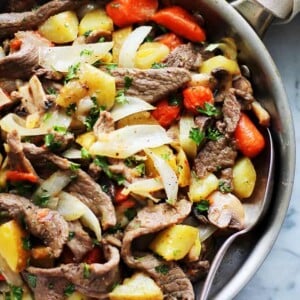 Close up overhead view of a steak and potatoes skillet on a marble countertop.