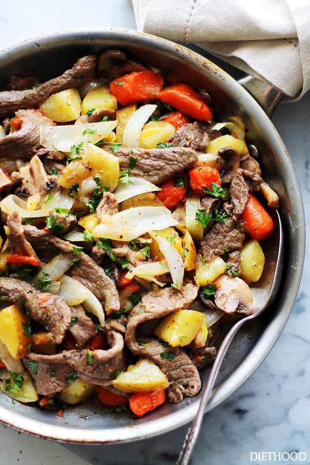 Close up overhead view of a steak and potatoes skillet on a marble countertop.