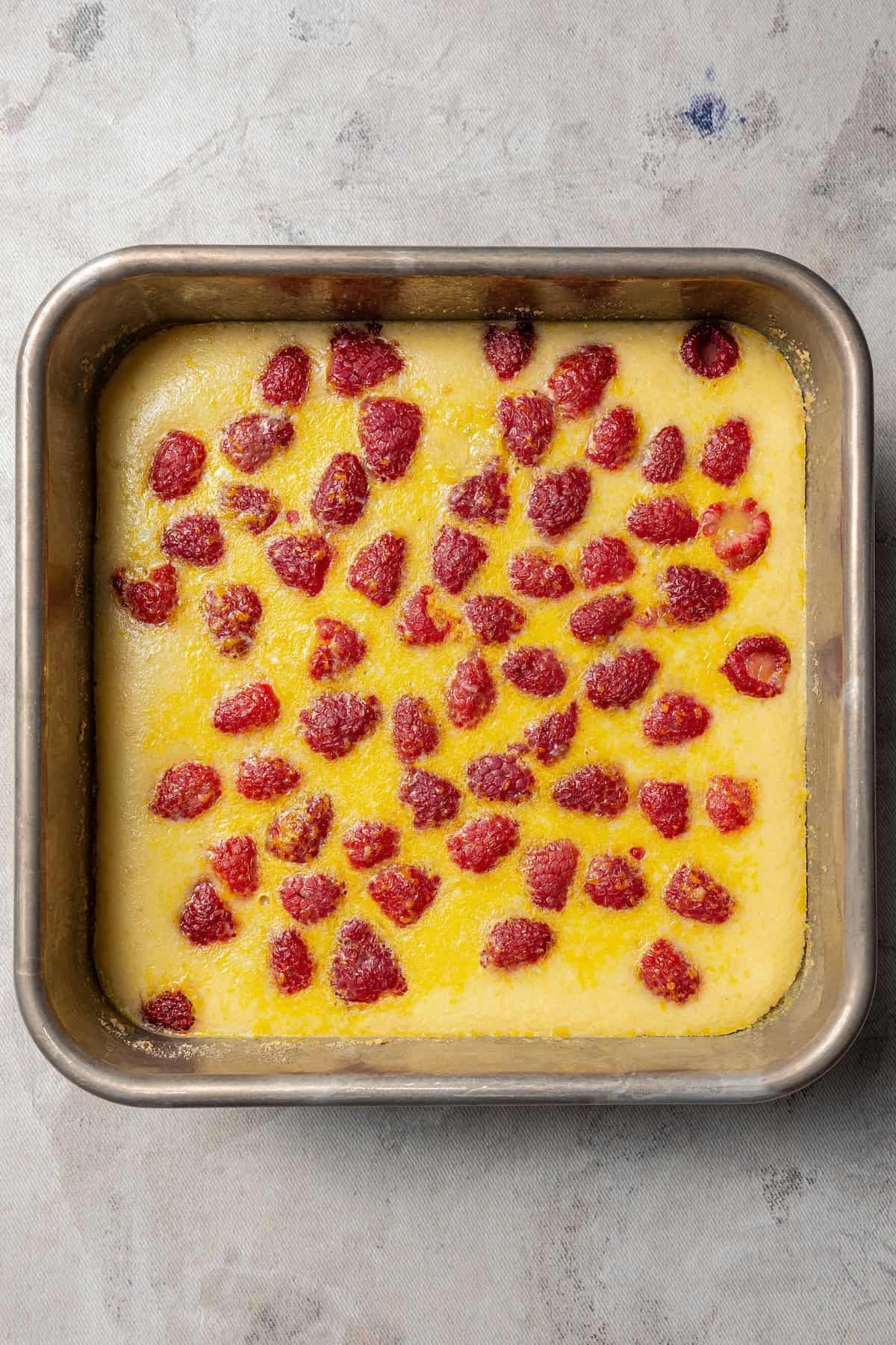 Lemon bar filling poured over fresh strawberries on top of a cookie crust in a baking pan.