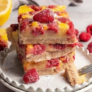 Three raspberry lemon bars stacked on a plate, dusted with powdered sugar.