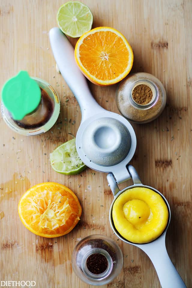 A manual citrus juicer surrounded by scattered halves of lemons, oranges, and limes on a wooden countertop.