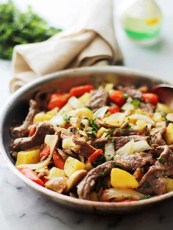 Steak and potatoes in a skillet on a marble countertop.