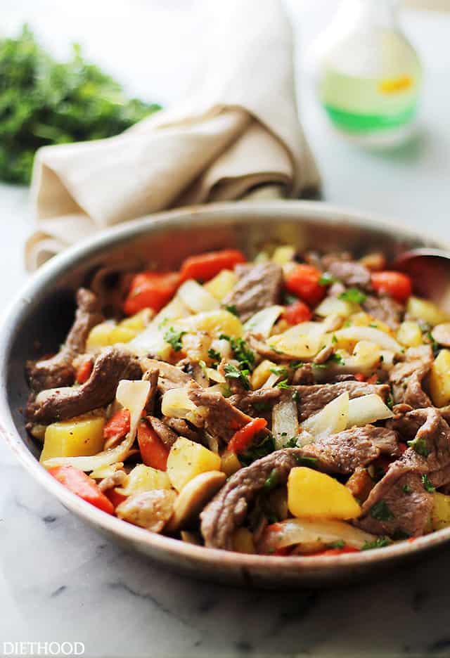 Steak and potatoes in a skillet on a marble countertop.