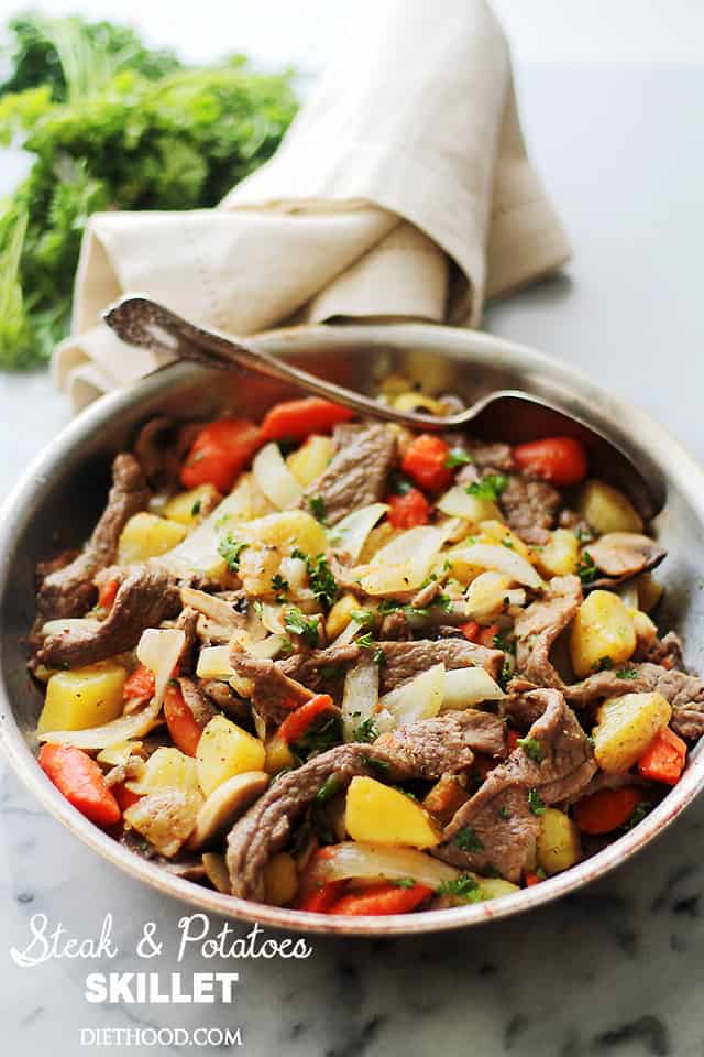 Steak and potatoes in a skillet on a marble countertop.