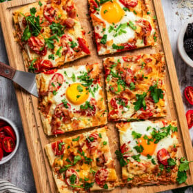 Sliced phyllo pizza with soft eggs, bacon, and tomatoes on a cutting board.