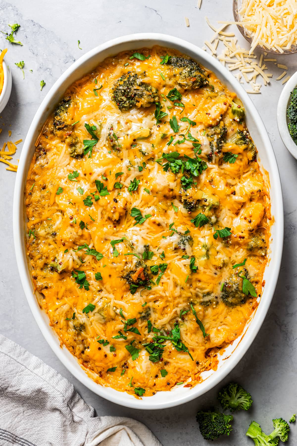 Overhead photo of chicken and broccoli casserole in a baking dish near a bowl of shredded cheese.