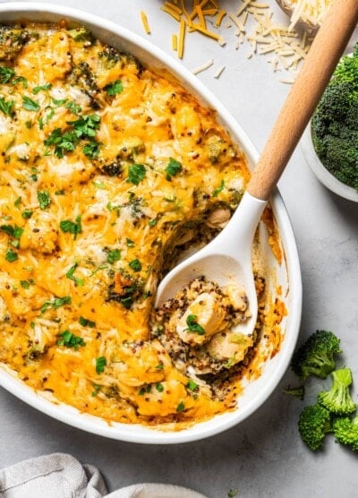 A serving spoon scooping out Chicken and broccoli from a casserole dish.