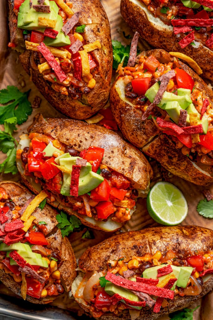 Close-up image of baked potatoes loaded with beans, avocado, cheese, tomatoes, and tortilla chips.