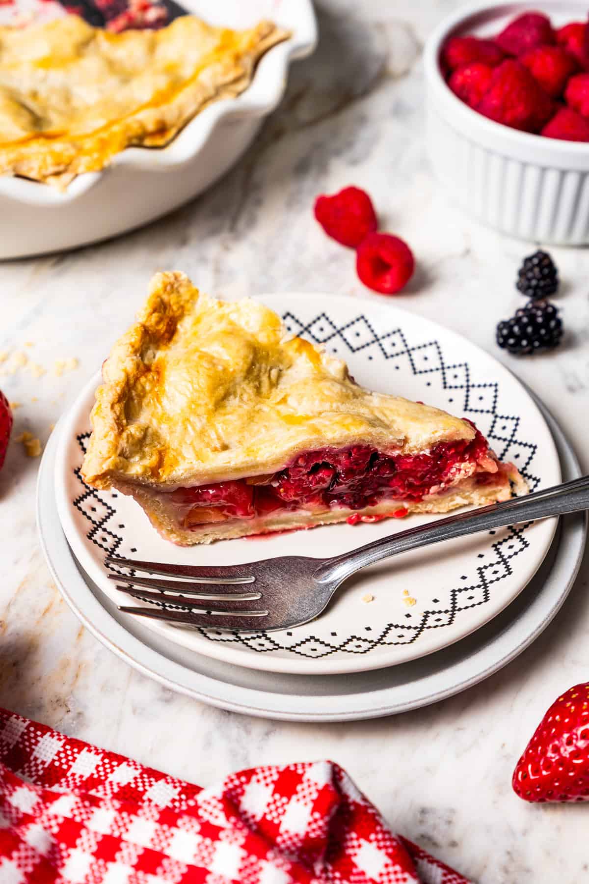 This easy mixed berry pie recipe combines three types of juicy berries with tender apples inside a light and flaky homemade pie crust. A slice of berry pie next to a fork on a plate.