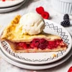 A slice of berry pie topped with a scoop of ice cream on a plate.