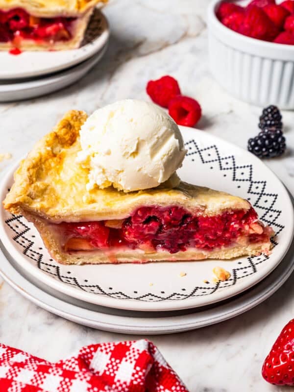 A slice of berry pie topped with a scoop of ice cream on a plate.