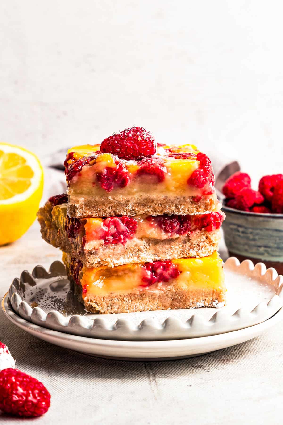 A stack of lemon bars studded with raspberries and served on a plate.