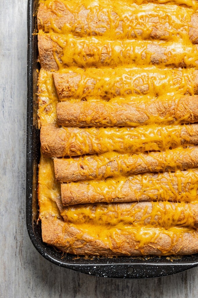 Enchiladas in the baking dish with melted cheese on top.