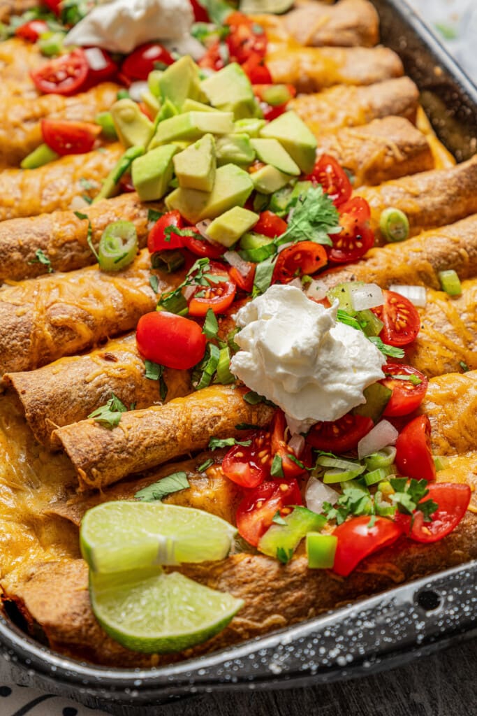 Breakfast enchiladas with sour cream, tomatoes, and avocado on top.