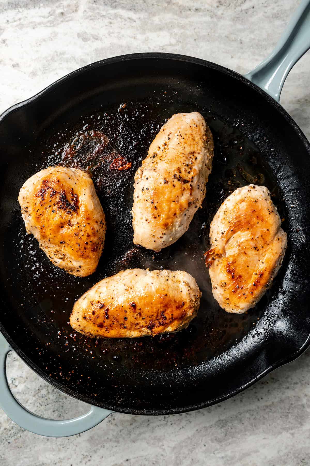 Four cooked seasoned chicken breasts in a cast iron skillet.