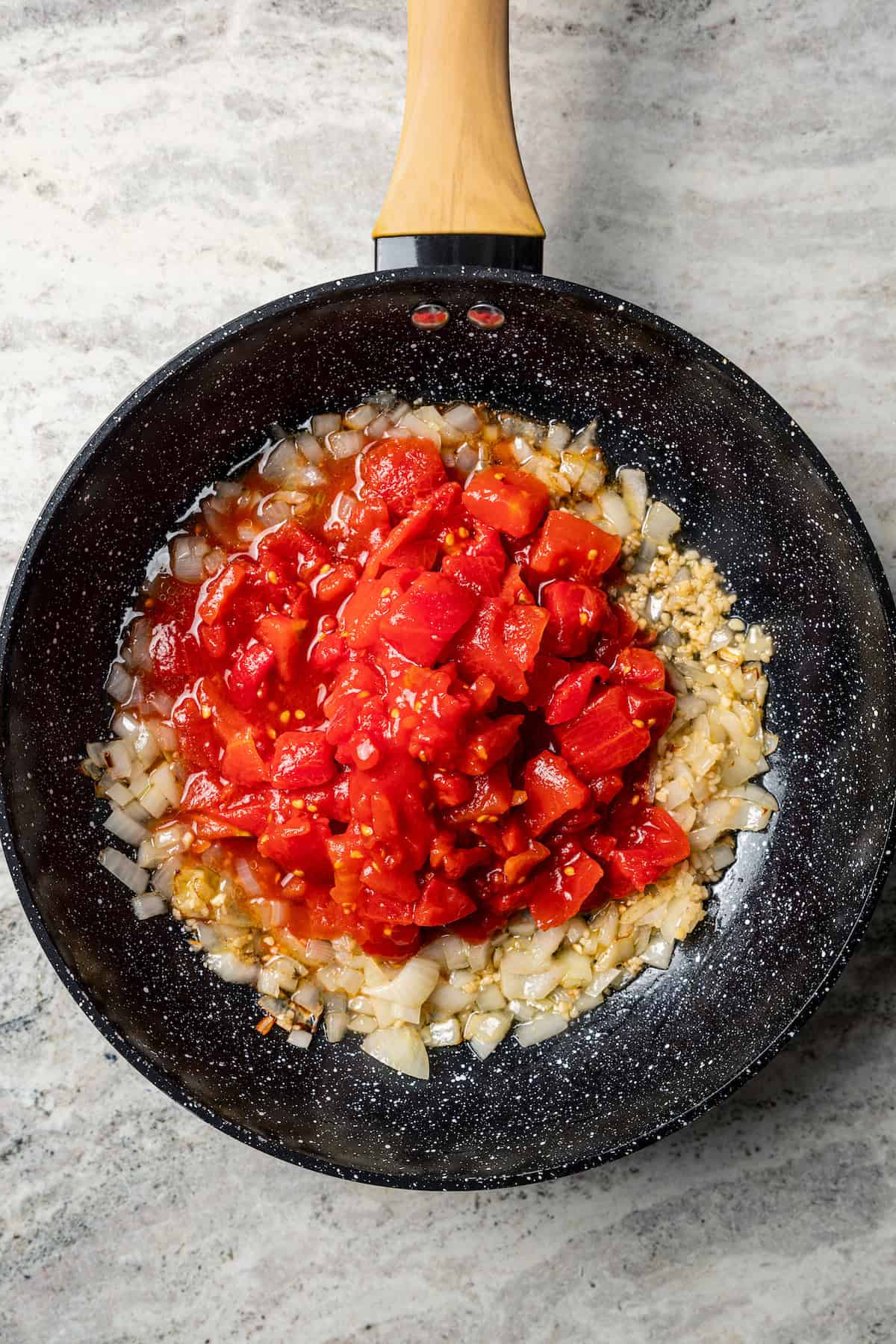 Diced tomatoes added to sauteed onions and garlic in a skillet.