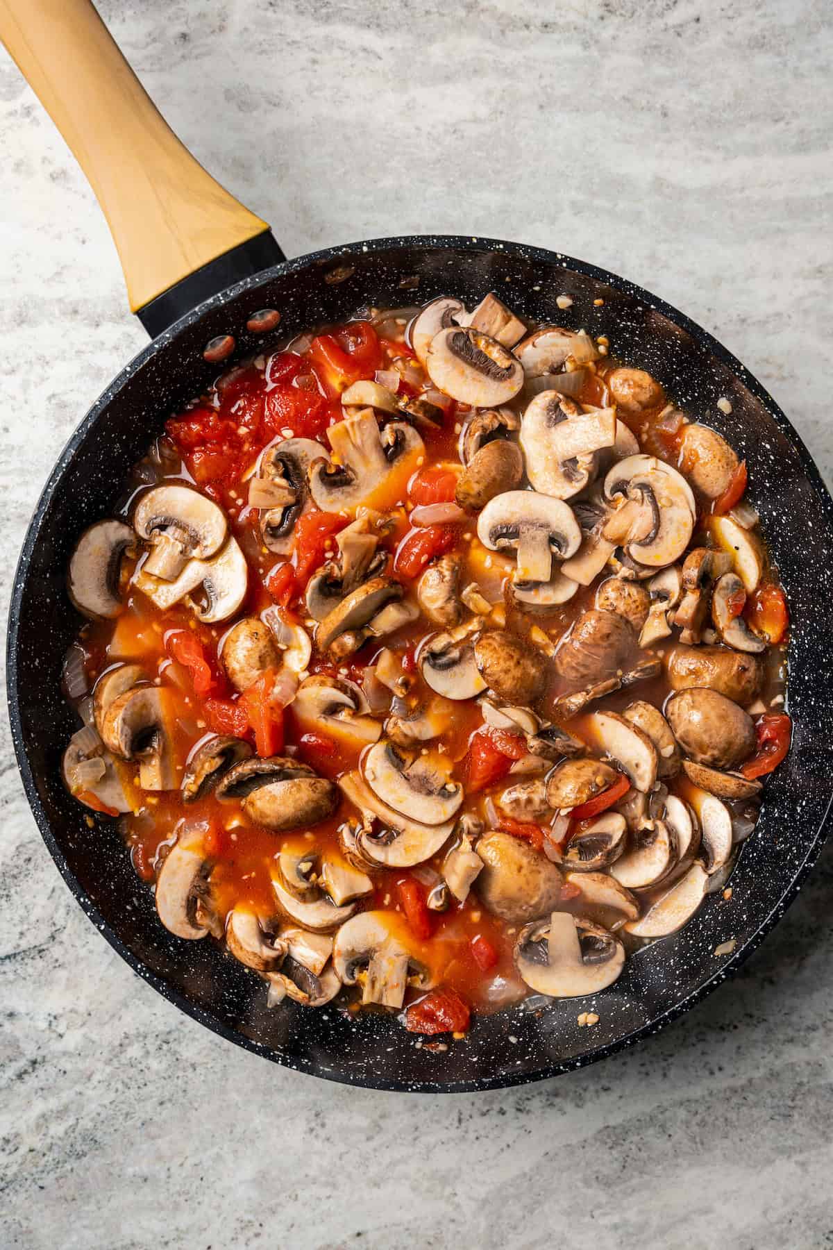 Sliced mushrooms added to tomato sauce in a skillet.