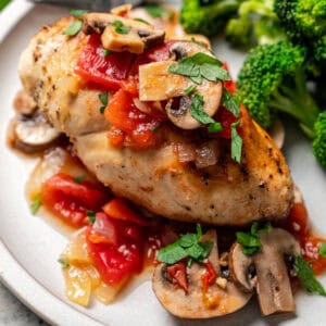 A serving of Chicken Marengo next to a side of steamed broccoli on a plate, with a fork in the background.