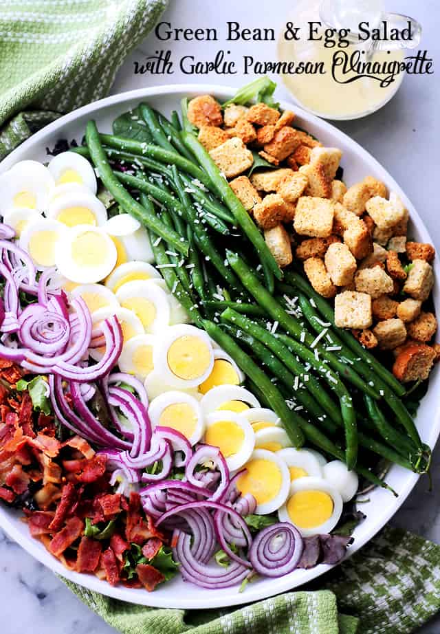 rows of green Beans, eggs, croutons, red onions, and bacon in a white serving plate.