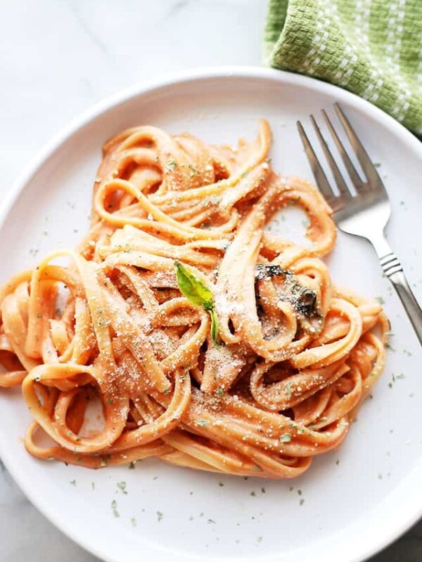 Cooked fettuccine pasta served on a dinner plate garnished with grated parmesan cheese and fresh basil leaves.