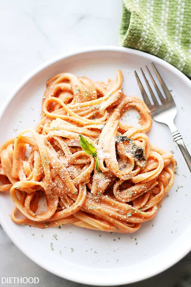 Fettuccine pasta served on a dinner plate and garnished with grated parmesan cheese plus fresh basil leaves.