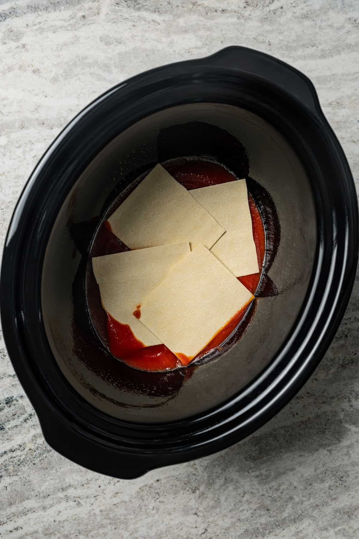 Lasagna noodles layered over marinara sauce in a crock pot.