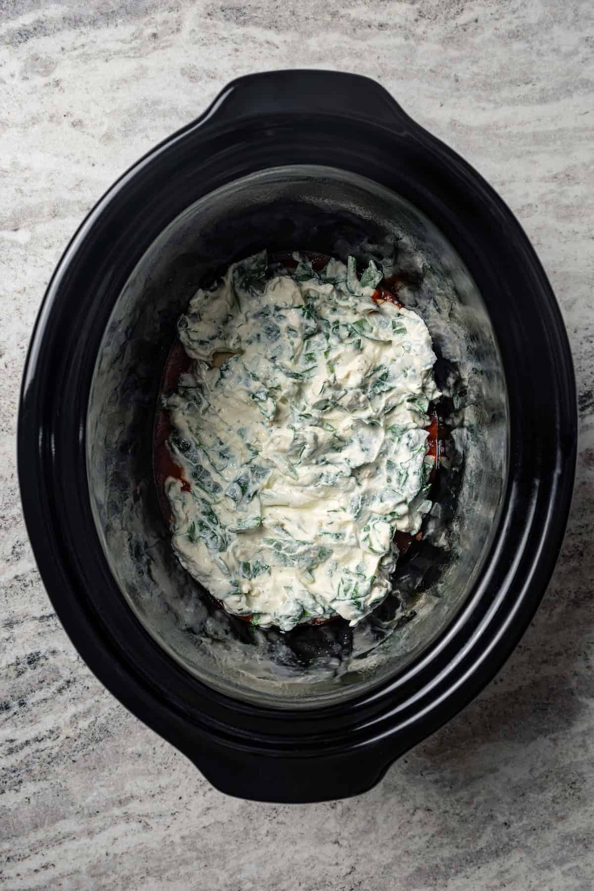 Cheesy spinach mixture layered into the crock pot.