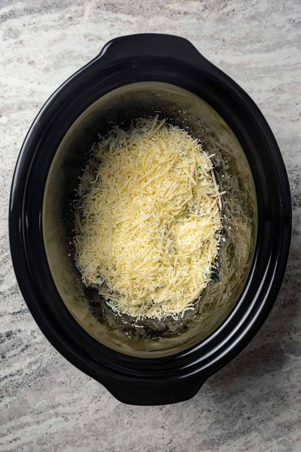 Shredded cheese layered over the ricotta and spinach mixture inside the crock pot.