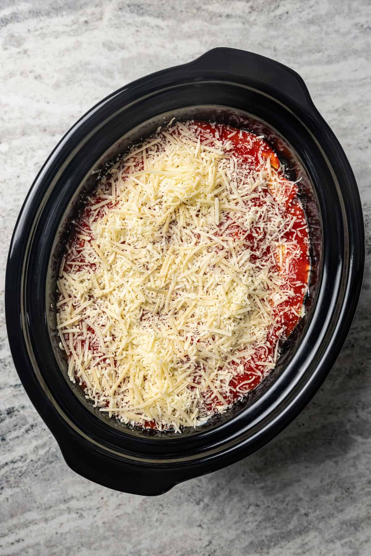 Spinach lasagna topped with freshly grated parmesan cheese inside the crock pot.