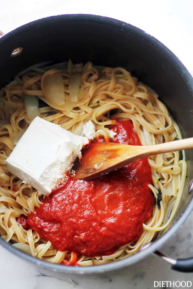 Stirring half of a block of cream cheese plus pasta sauce into cooked fettuccine.