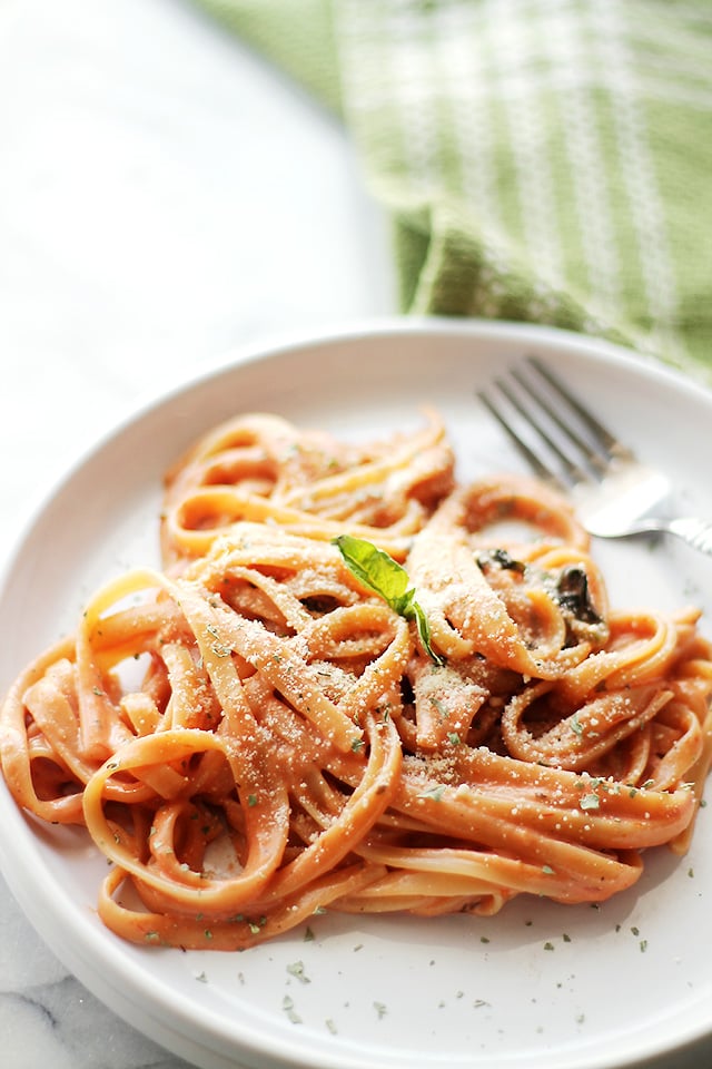 Pasta served on a dinner plate and garnished with fresh basil and grated parmesan.