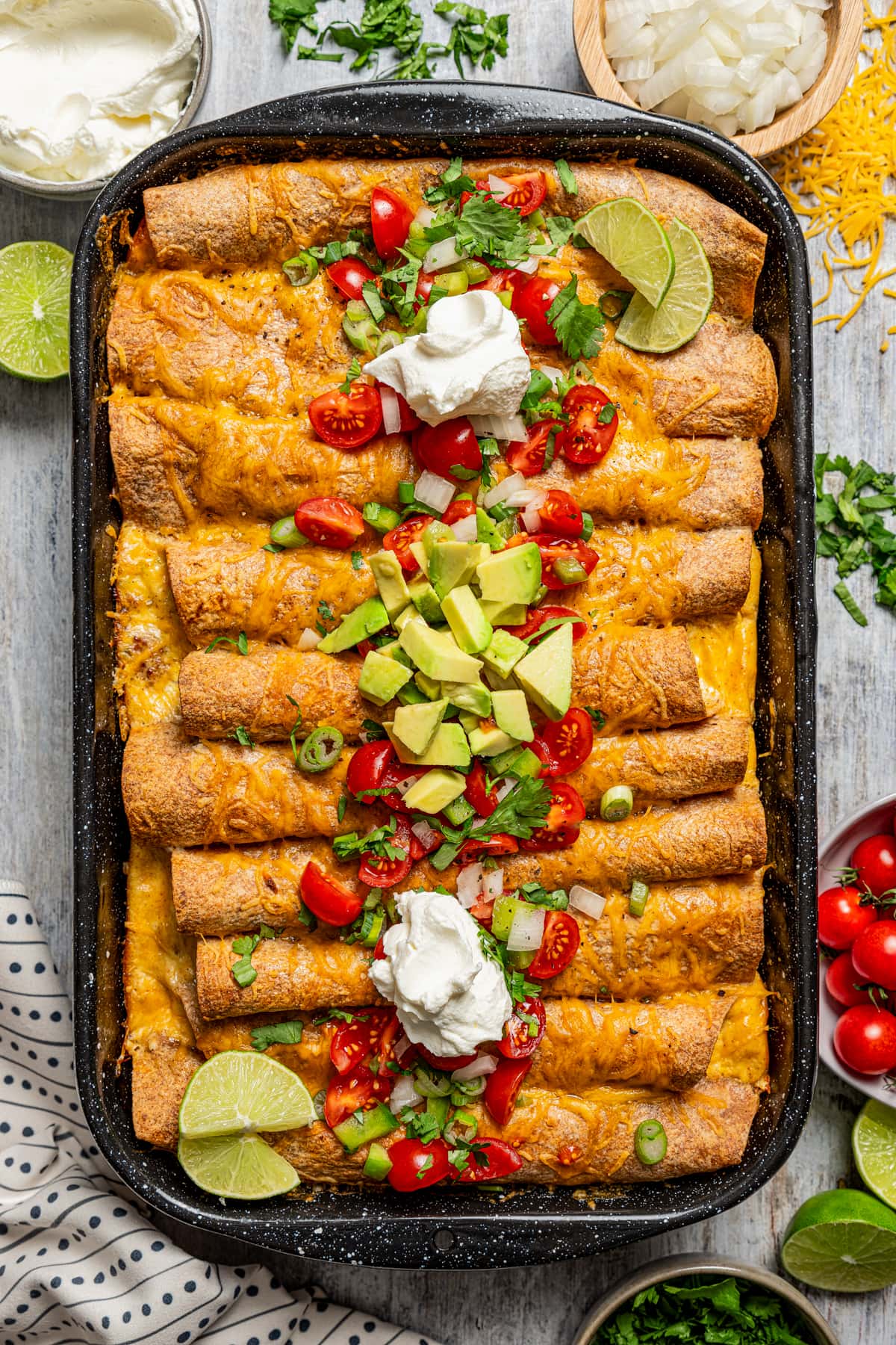 Enchiladas in the baking dish with cilantro, sour cream, tomatoes, chilis, and avocado.