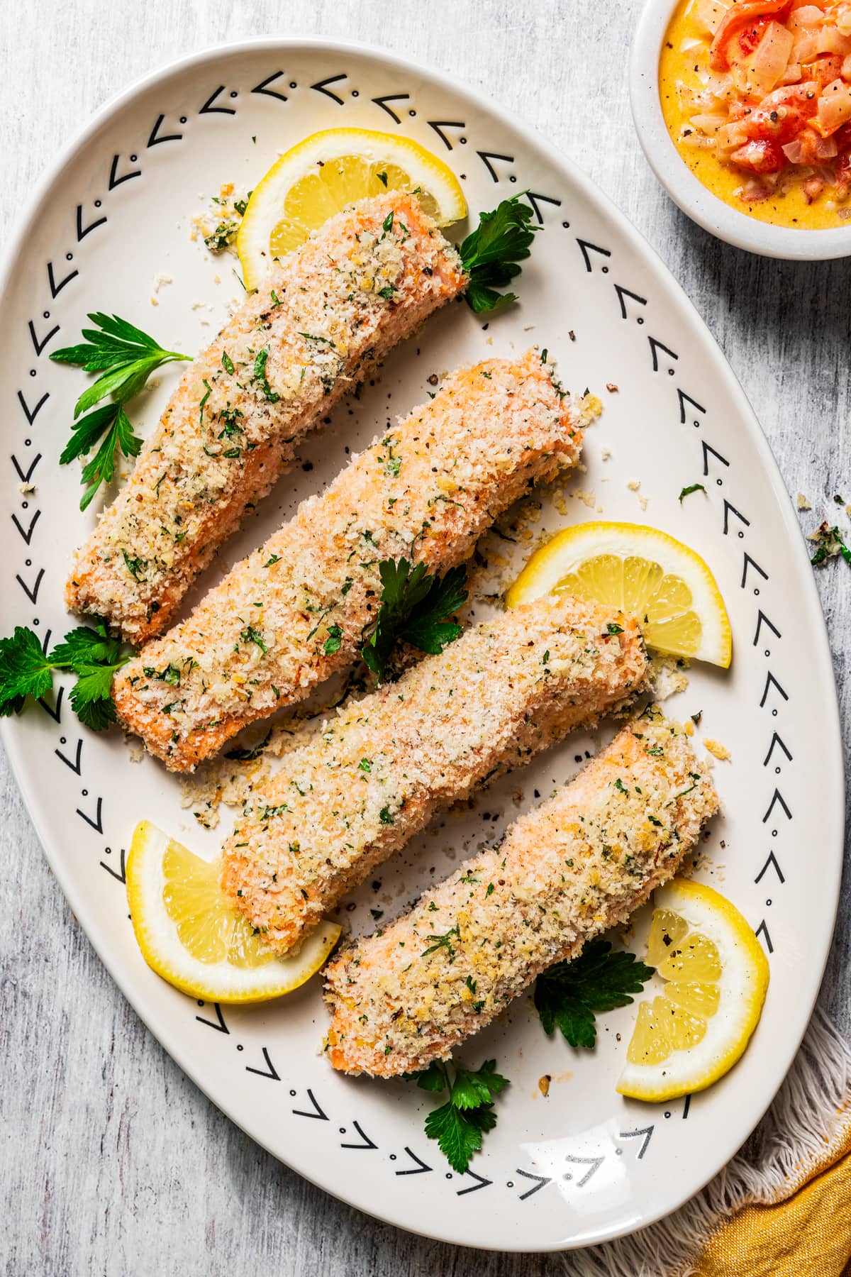 Four panko-crusted salmon filets on a platter garnished with parsley and lemon wedges.