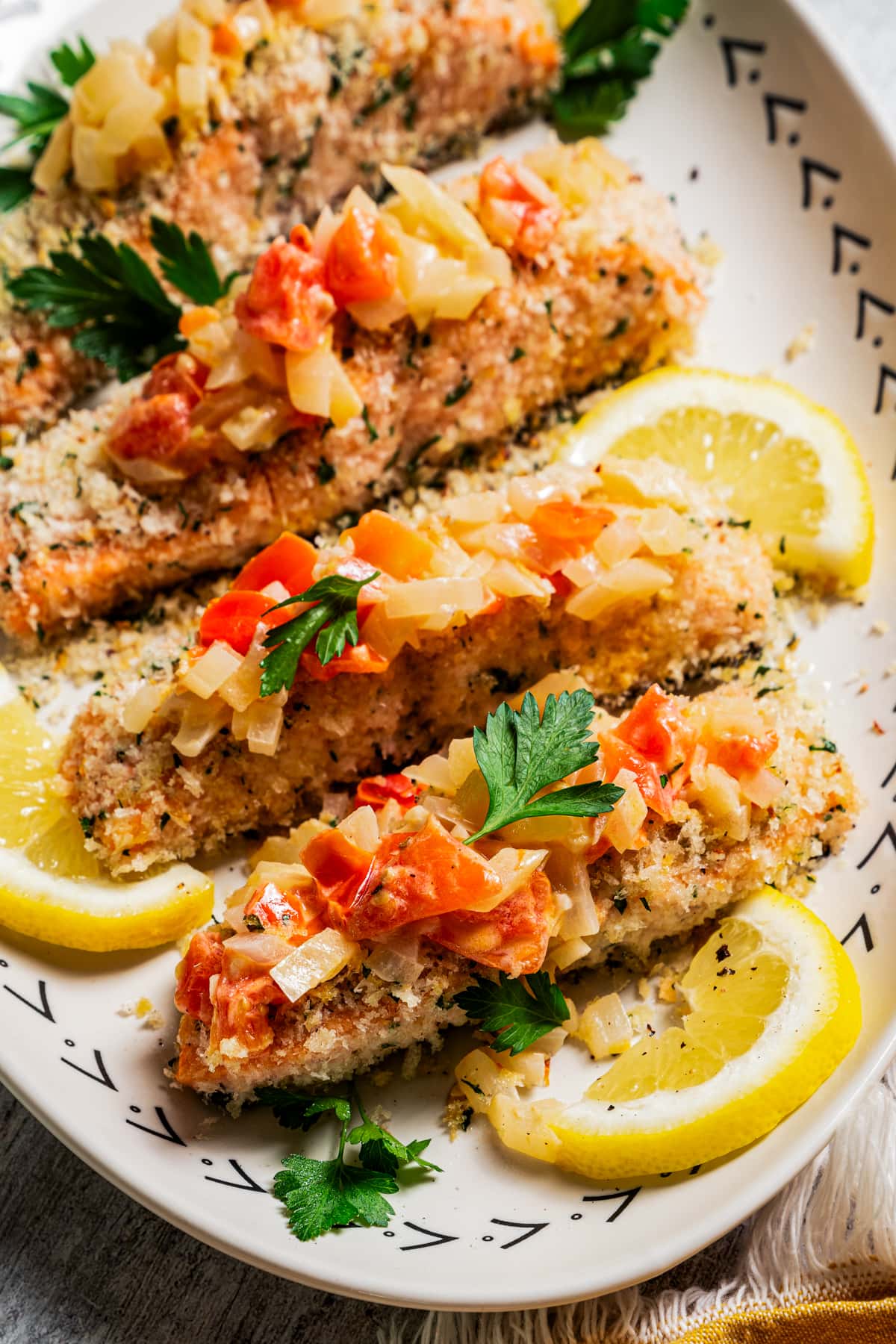 Panko-crusted salmon filets on a platter next to a lemon wedge, topped with Tuscan tomato sauce.