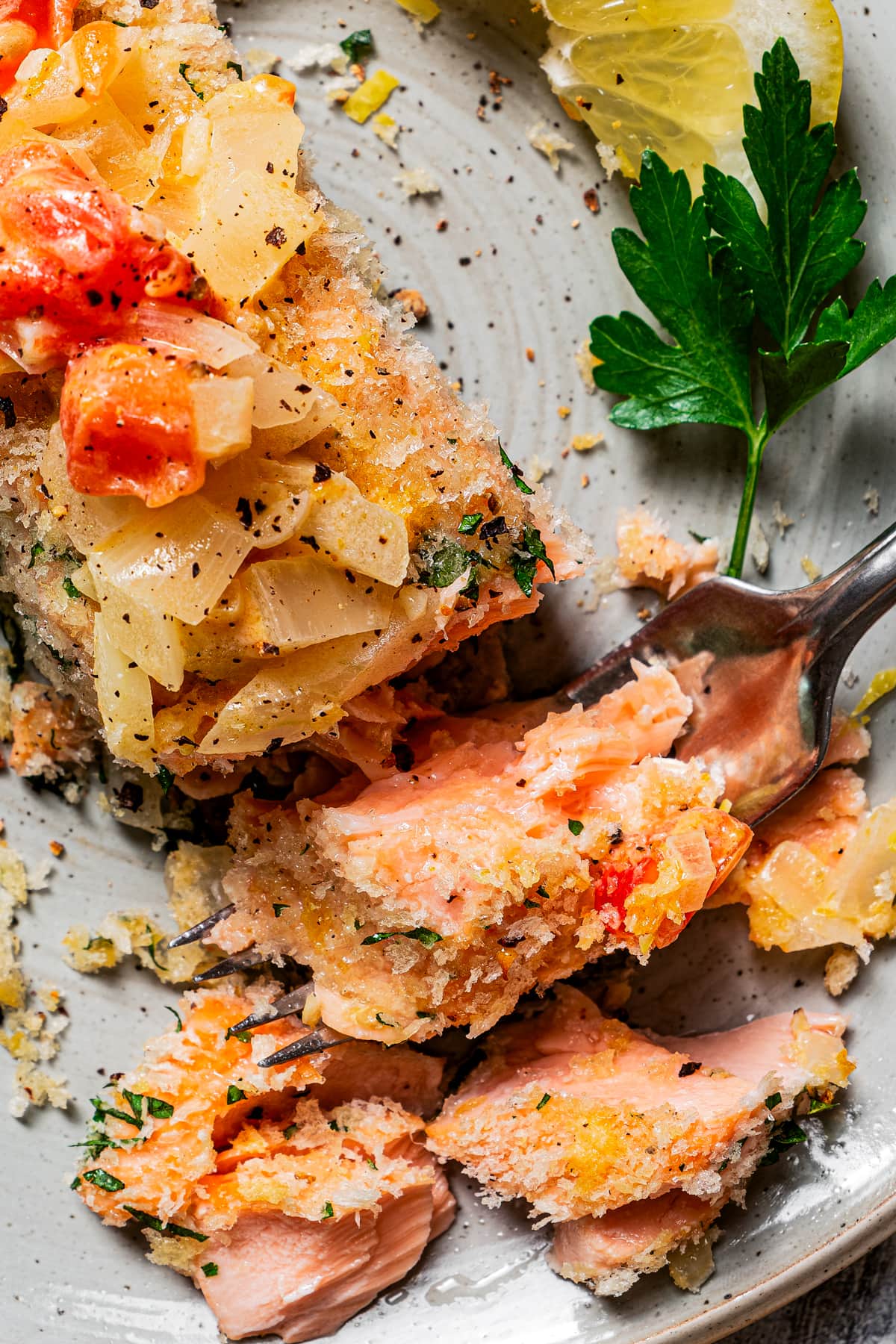 Overhead close-up photo of a fork scooping out a bite from a panko-crusted salmon fillet topped with tomato sauce.