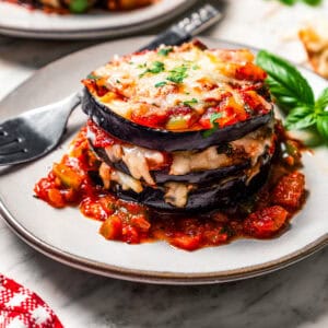 Roasted eggplant stacked with tomato sauce and cheese on a plate, with a second plate in the background.