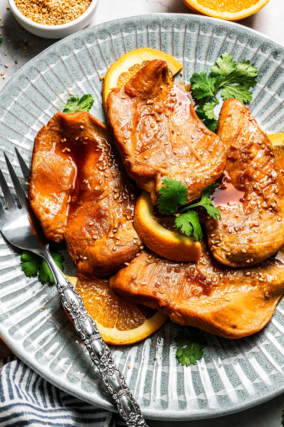 Crockpot orange chicken breasts arranged on a plate with a fork.