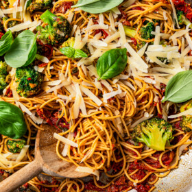 Close-up image of pasta in a skillet tossed with cheese, tomatoes, broccoli, and basil.