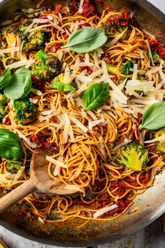 Close-up image of pasta in a skillet tossed with cheese, tomatoes, broccoli, and basil.