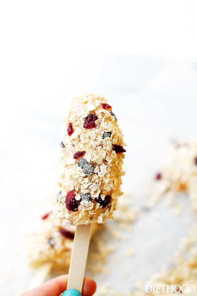 A hand holding up a banana popsicle coated with yogurt and granola.