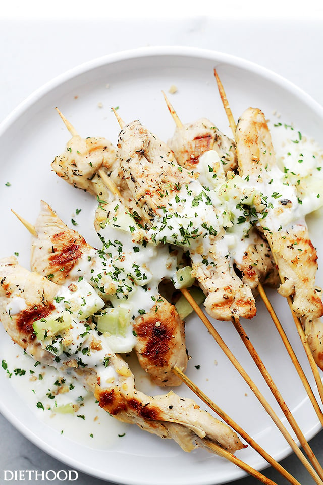 Chicken Skewers topped with Cucumber-Garlic Yogurt Sauce on a white plate.