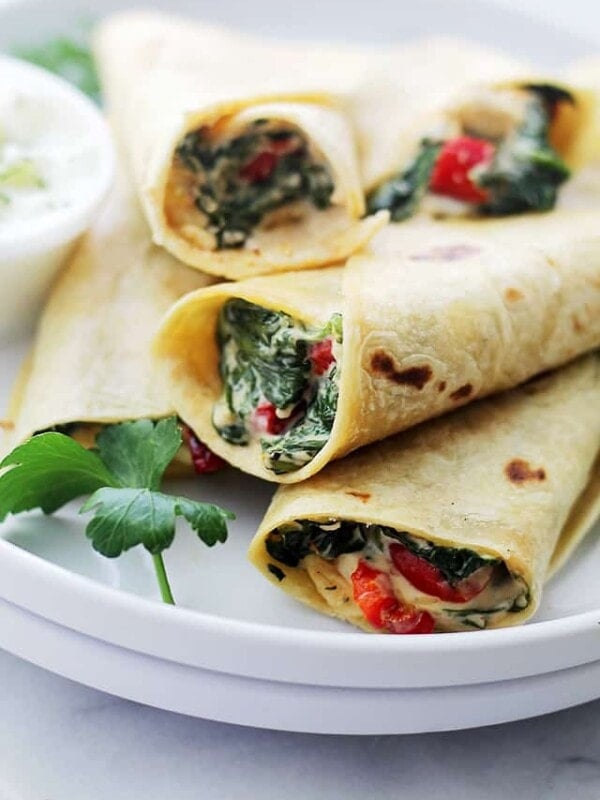 Assorted spinach feta wraps stacked on a white plate.