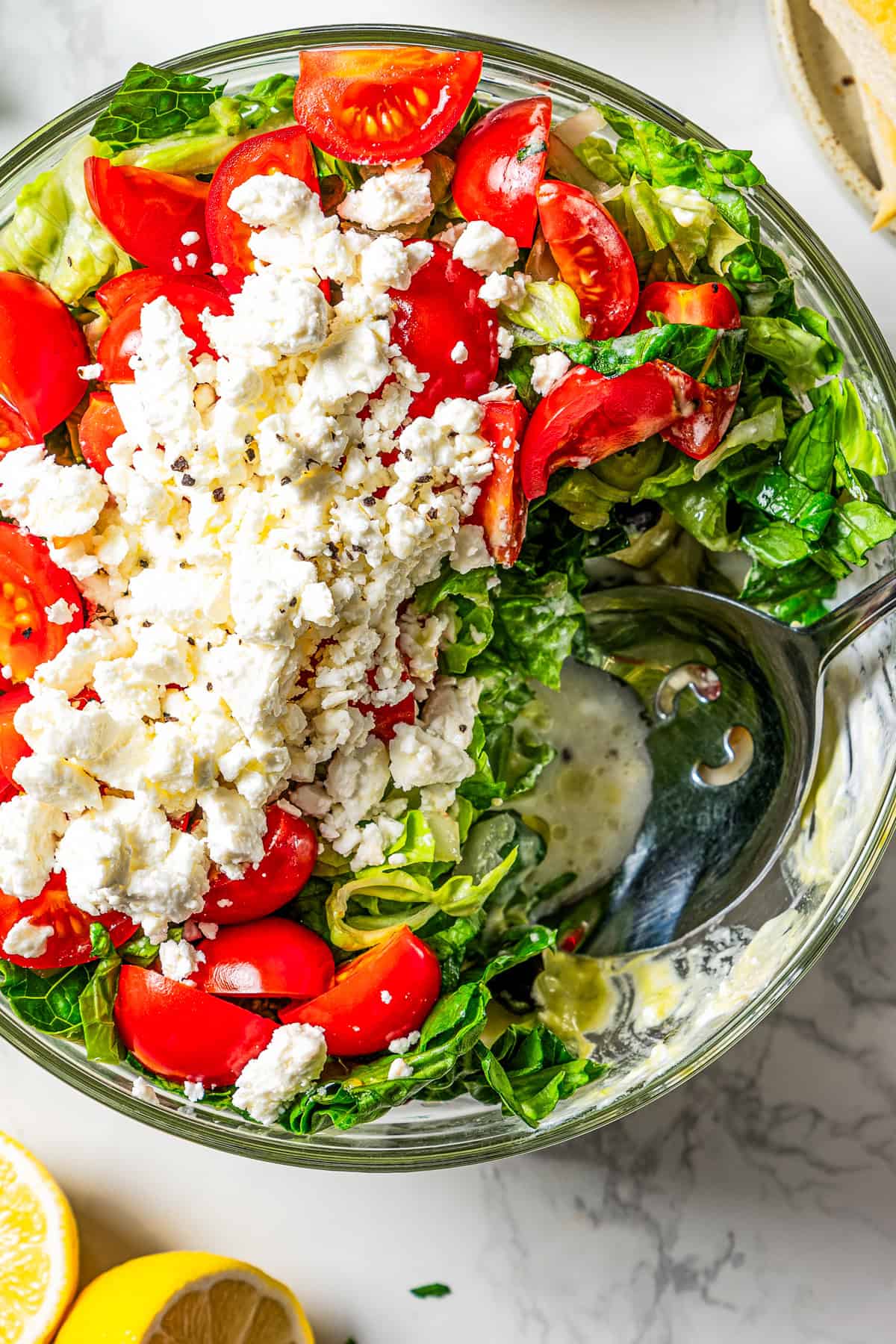 Mediterranean seven layer dip in a glass bowl with a serving spoon resting inside the bowl.