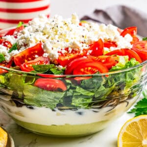 Side view of Mediterranean seven layer dip in a glass bowl, showing the different layers.