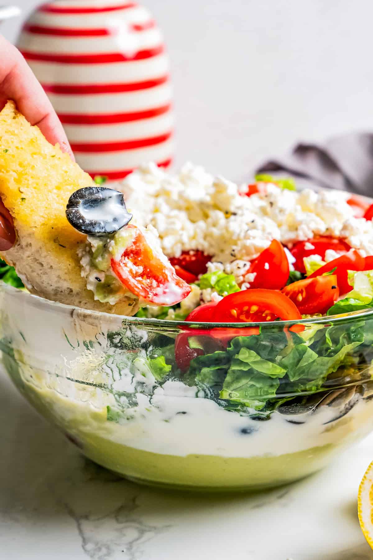 A hand dipping a corn chip into a bowl of Mediterranean seven layer dip.