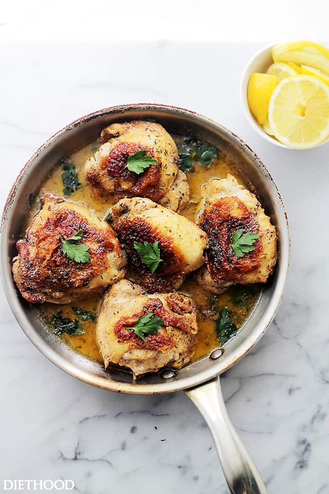 Cooked chicken thighs in a pan topped with parsley.