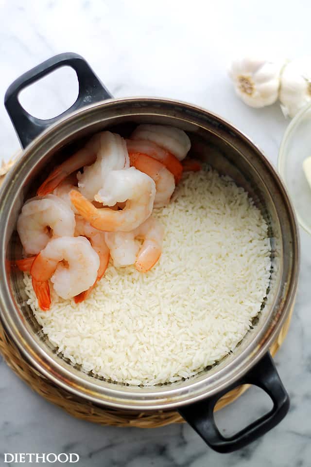 Cooked white rice in a saucepan with several cooked shrimp arranged on top of the rice.