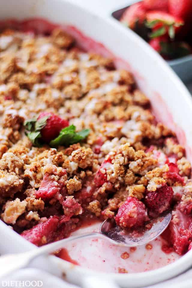 Strawberry crumble in an oval baking dish with a spoon resting in the space where a few scoops are missing.